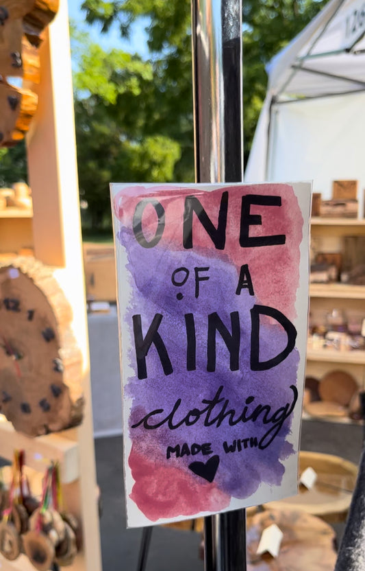 One of a kind clothing made with love text on pink and purple water color background on a pole.